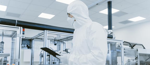 An operator wearing full coverall standing up in a cleanroom with a notepad.