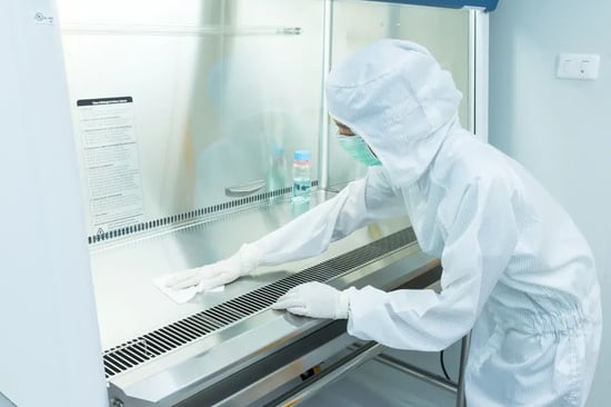Cleanroom technician in full bunny suit and gloves wiping the interior surface of a cleanroom.