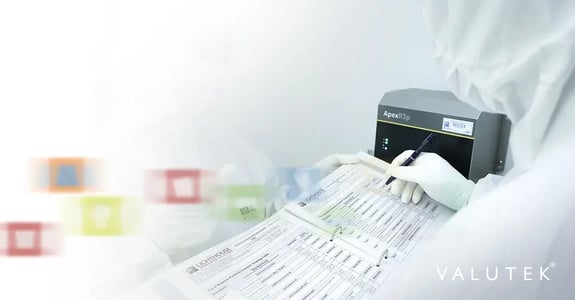 A cleanroom technician in full gowning records data on a monitoring sheet, with a particle counter device visible in the background.