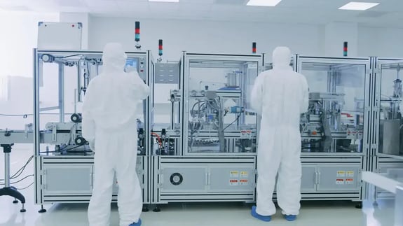 Cleanroom technicians wearing contamination control apparel working in pharmaceutical or semiconductor manufacturing environment.
