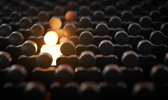 A glowing figure stands out among a crowd of identical dark silhouettes, symbolizing individuality.
