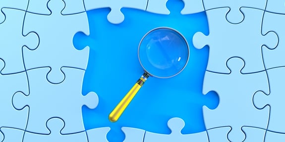 Image of a blue puzzle piece with a magnifying glass focusing on it.