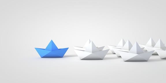 A blue origami boats leads the other origami boats.