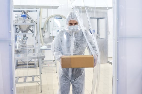 Pharmaceutical cleanroom operator carrying cardboard box.