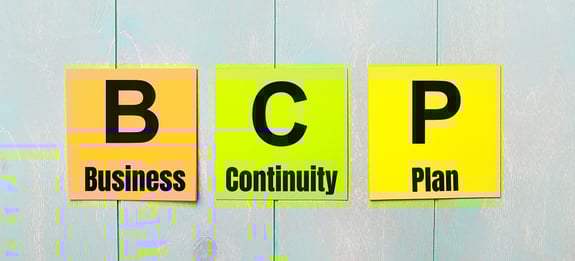 Image of three colored stickers with the text 'BCP' (Business Continuity Plan) on a light blue wooden background.